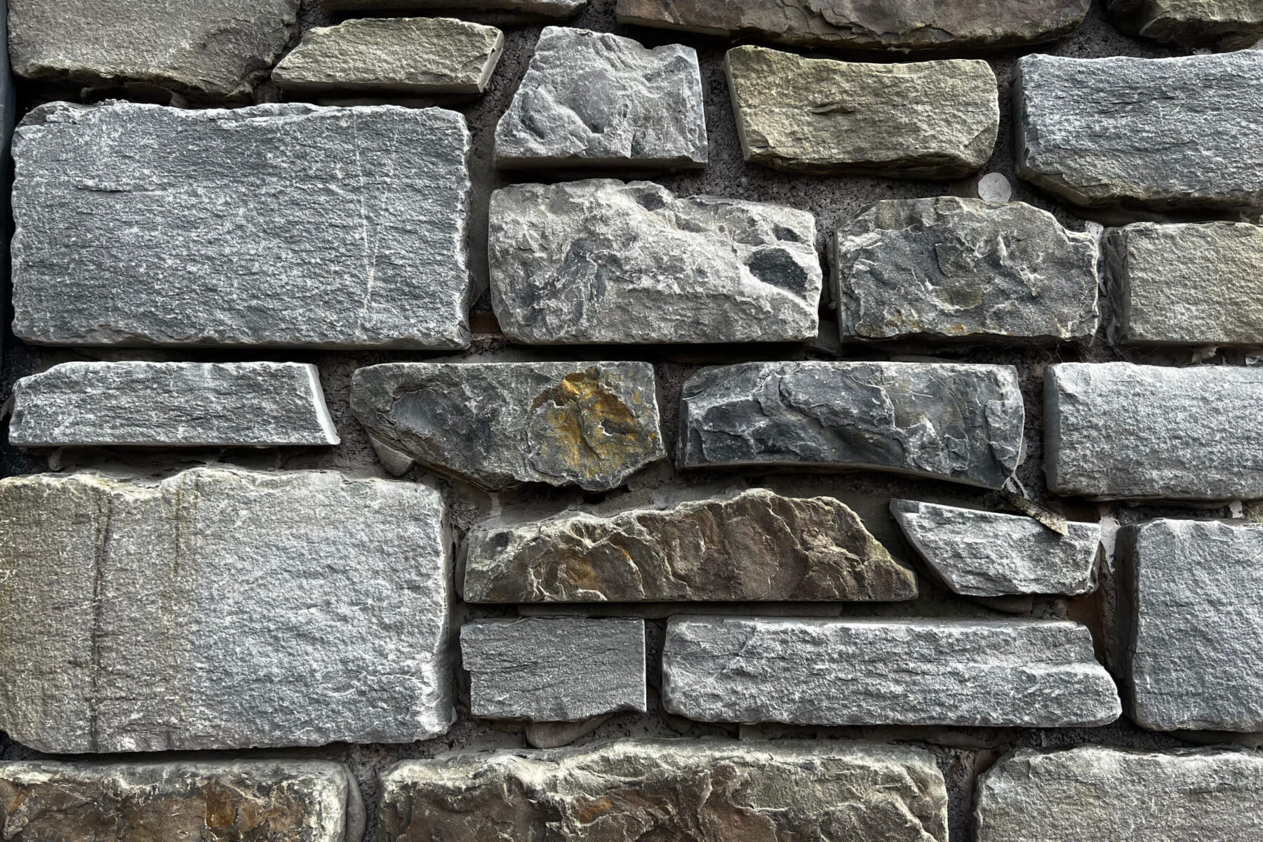 Natural stone wall with varied gray and blue-toned rough-cut stones arranged in horizontal courses with mortar joints